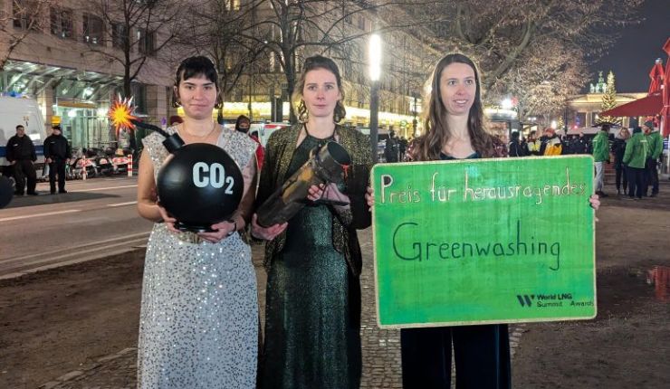 Drei Personen in Abendkleidern mit einer CO2-Bombe, einer blutigen Pipeline und einem grünen Schild "Preis für herausragendes Greenwashing"